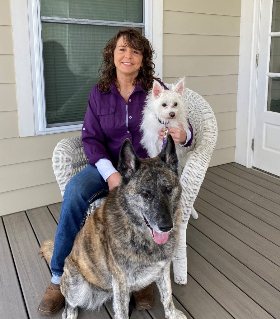 Susan sitting in a rocking chair on a porch at TROSA's campus, with her two dogs.