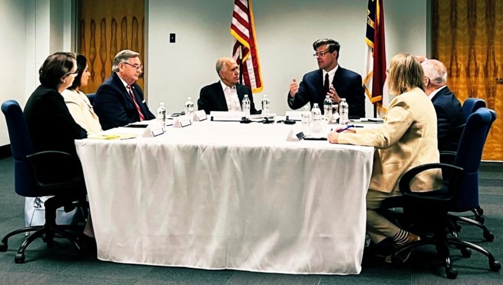 Kody Kinsley, Secretary of the North Carolina Department of Health and Human Services; Dr. Timothy Reeder and Senator Jim Burgin from the NC General Assembly; Dr. Robyn Jordan from the NC Medical Society; Stephen Lawler from the NC Healthcare Association; and Dr. Ripple Sekhon with the United States Department of Veteran Affairs, seated around a table engaged in discussion.