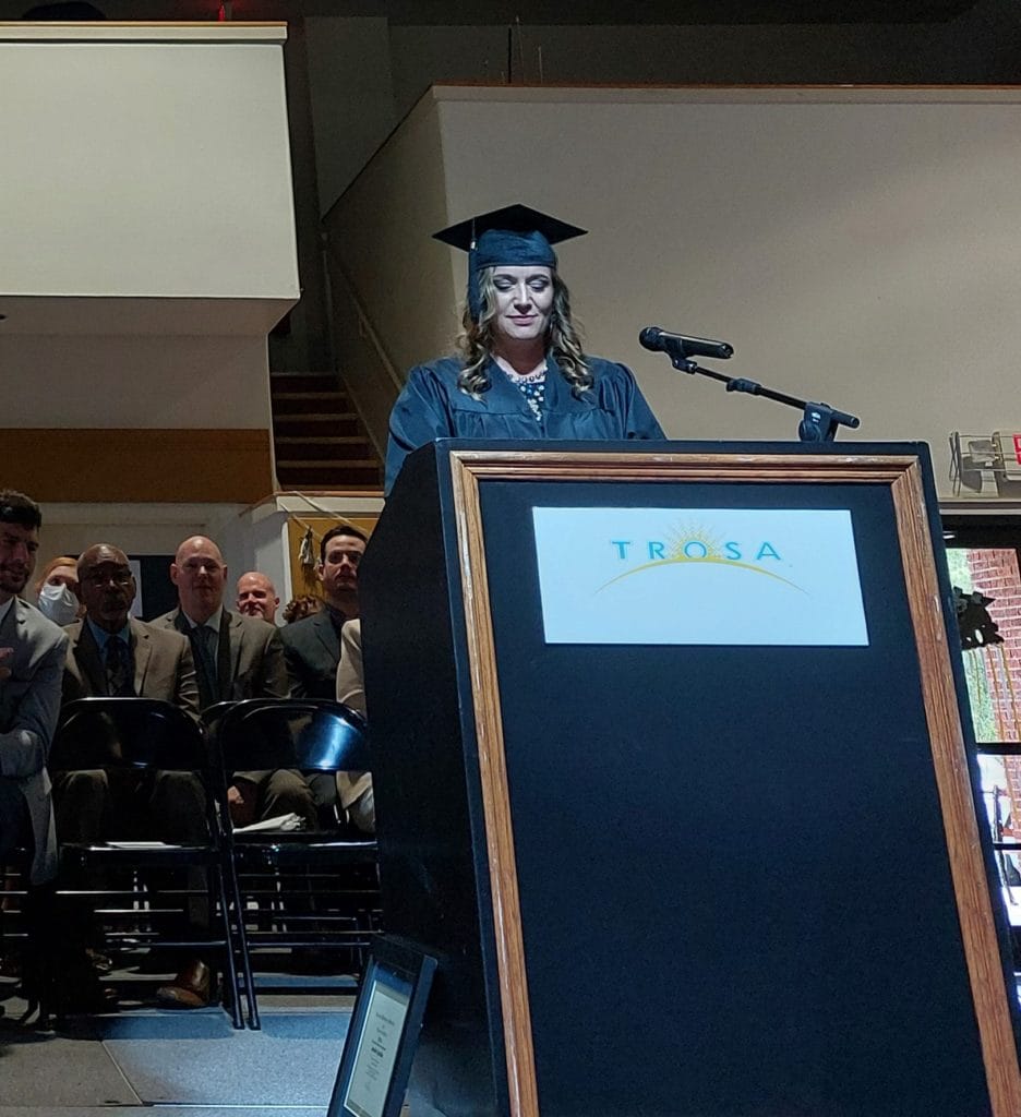 TROSA program graduate Jennifer stands at podium in TROSA gymnasium